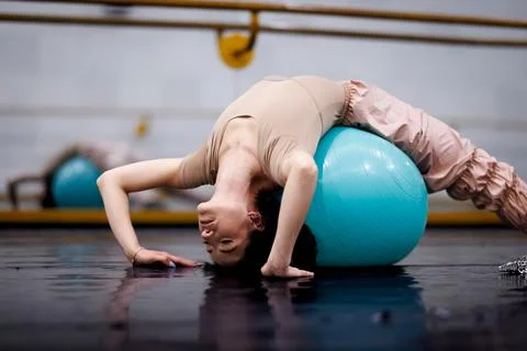 Dancer practices acrobatic moves on a blue exercise ball in a dance studio Stock Photos