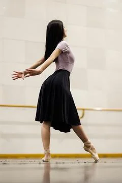 Dancer practices in a studio with a mirrored wall and a ballet bar while Stock Photos