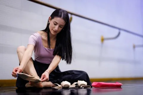 Dancer prepares ballet shoes in studio during class sitting on floor with shoes Stock Photos