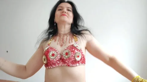 A dancer in a red suit is dancing an oriental dance on a white background. A Stock Footage 268158339