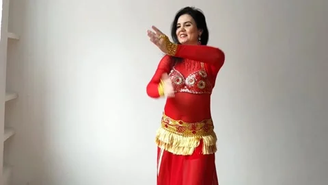A dancer in a red suit is dancing an oriental dance on a white background. A Stock Footage 273660409