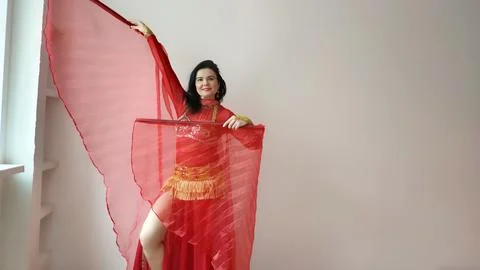 A dancer in a red suit is dancing with a red wings an oriental dance on a white Foto stock
