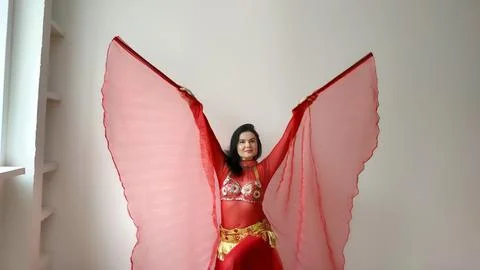 A dancer in a red suit is dancing with a red wings an oriental dance on a white Stock Photos