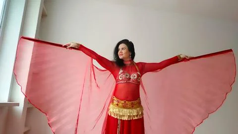 A dancer in a red suit is dancing with a red wings an oriental dance on a white Foto stock