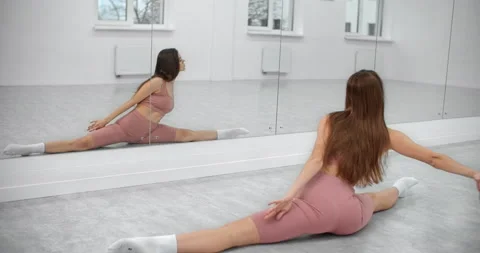 Dancer is sitting on the twine and warming up infront of the mirror wall in the Stock Footage 145616558