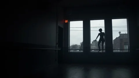 Dancer on window sill dancing in large dark moody dance studio 스톡 동영상 104275354