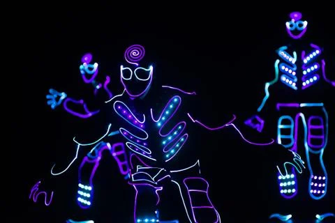 Dancers in led suits on dark background, colored show Stock Photos