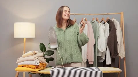 Dancing delighted brown haired young woman wearing knitted shirt ironing clothes Видео 259081481