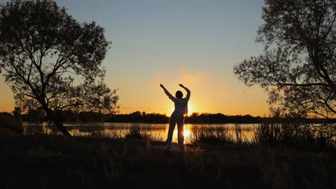Dancing joyfully by the lake as the sun sets in a serene outdoors setting Stock Footage 346721754