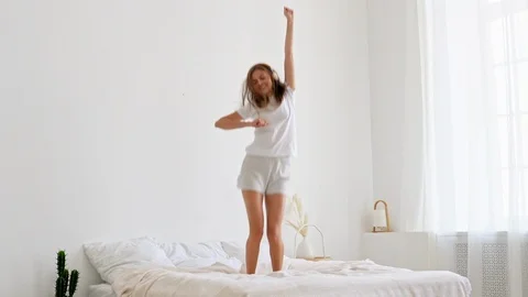 Dancing young woman jumping on bed at home, wearing headphones Stock-Footage 125851580