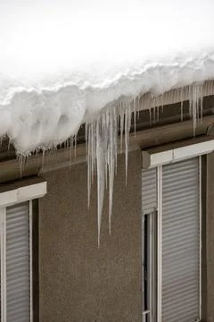 Dangerous sharp icicles on edge of street building roof covered with snow Stock Photos