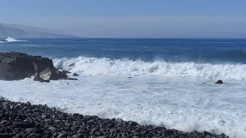 Dangerous waves hit some retaining rocks and the shore of a volcanic beach Stock Footage 201935866