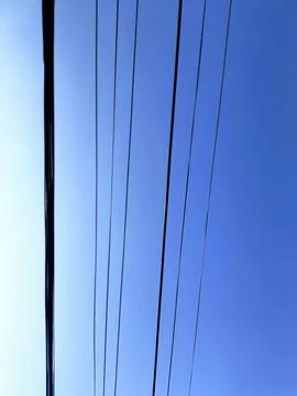 Dangling telecommunication and power cables set against a clear blue sky. Stock Photos