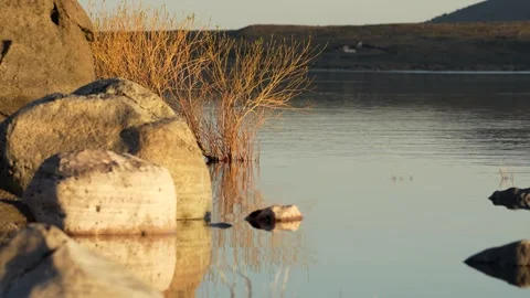 Dappled light effect is seen projected on the rocks on the shores of a lake.. Stock Footage 289688637