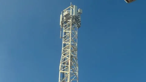 A daring worker ascends a towering cell phone tower against a clear blue sky. Stock Footage 294165613