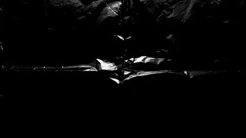 Dark abstract texture with crumpled black plastic wrap reflecting bright st.. Foto stock