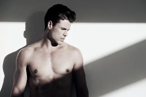 Dark and brooding. a handsome young man with no shirt on standing in the shadows Fotos de archivo