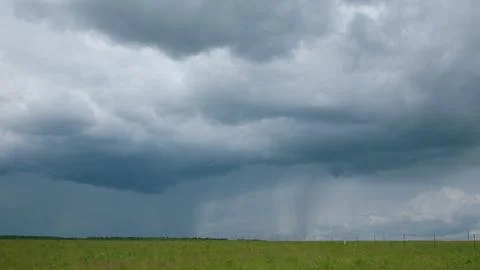 A dark and cloudy sky is filled with rain showers gently falling over vibrant gr 스톡 사진