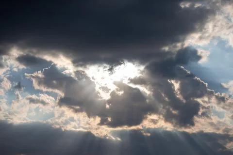 Dark and light clouds create a striking contrast in the sky, with sunlight pi Stock Photos