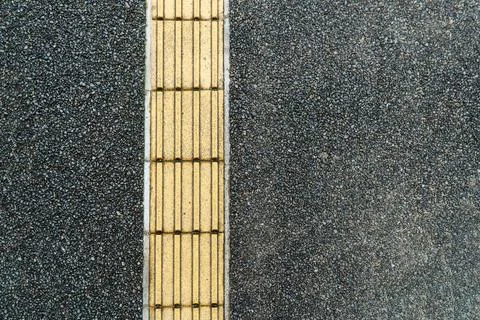 Dark Asphalt Path with a Yellow Tactile Paving Guide Strip 写真素材