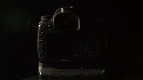 Dark back of DSLR camera revolves on black background, side lighting Stock Footage 333475170