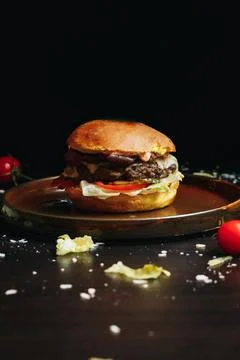 Dark backdrop shows burger on round wooden serving platter Stock-Fotos