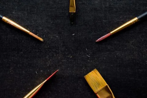 Dark background with different size golden paint brushes - concept of art suppli Stock Photos