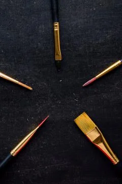 Dark background with different size golden paint brushes - concept of art suppli Stock Photos