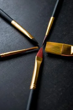 Dark background with different size golden paint brushes - concept of art suppli Stock Photos