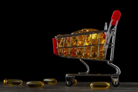 Dark background image with a toy shopping cart filled with omega-3 fish oil p Stock Photos