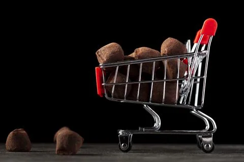 Dark background image with a toy shopping cart filled with chocolate truffles Stock Photos