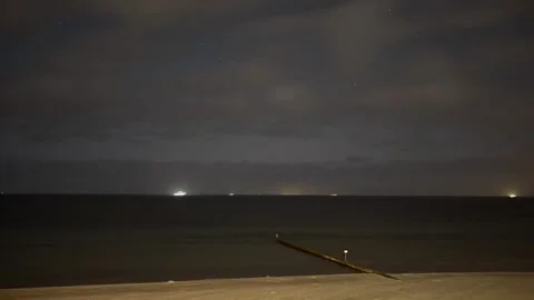 Dark beach at night with a cloudy sky and ship lights on the horizon, timelaps Stock Footage 334347494