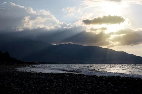 Dark beach with sunrays breaking through clouds Stock Photos