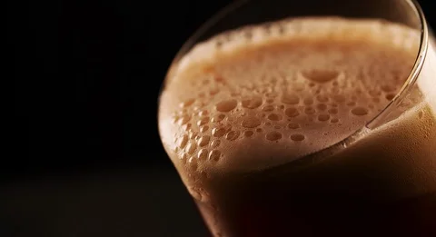 Dark Beer is Foaming and spilling out of glass closeup Slow motion video Stock Footage 103637869
