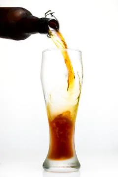 Dark beer is pouring from a bottle into a misted beer glass on a white backgr Stock Photos