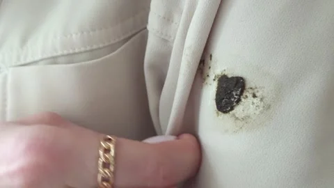 Dark bird dropping stain on beige fabric clothing, finger pointing at the dir 库存影片 336274373