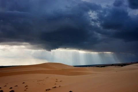 Dark black storm clouds with piercing sunrays covering desert landscape. Stock Photos