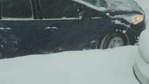 Dark blue car stuck in deep snow, wheel spinning, during severe winter snowstorm Stock Footage 347581006