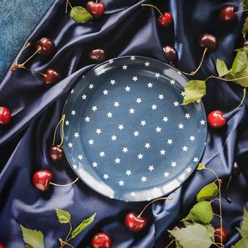 Dark blue composition with an empty blue plate with a star pattern and cherries Stock Photos