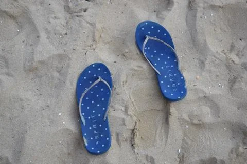 Dark blue dotted flip-flops on sand Stock Photos