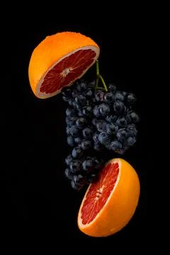Dark blue grape with red grapefruit on black background Stock Photos