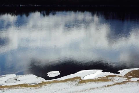 Dark blue river reflection of clouds and trees first snow on the beach Stock Photos