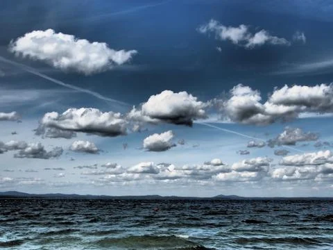 Dark blue sky with white cumulonimbus clouds over morning lake Stock Photos