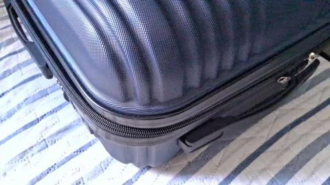 Dark blue textured hard shell suitcase resting on a striped bed Stock Photos