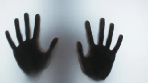 Dark blurry silhouette of two hands pressing against a frosted glass Stock Footage 327158432