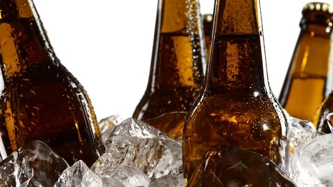 Dark bottles of beer are in a container with ice pieces. White background. Close Stock Footage