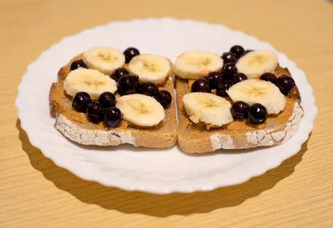 Dark bread with peanut butter, black currant and banana slices Stock Photos