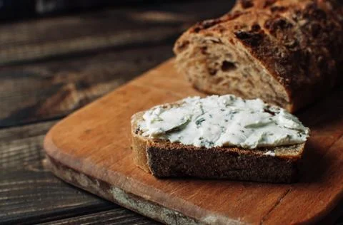 Dark bread is spread with cottage cheese with herbs in a cut on a wooden boar Foto stock
