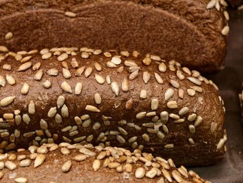Dark brick shaped bread covered with sunflower seeds, arranged among bakery.. Stock Photos