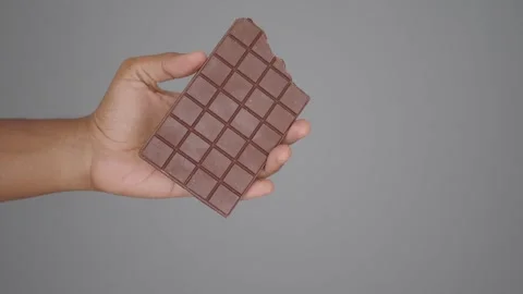 Dark brown chocolate bar held by hand against gray background showing squar.. Stock Footage 332033982